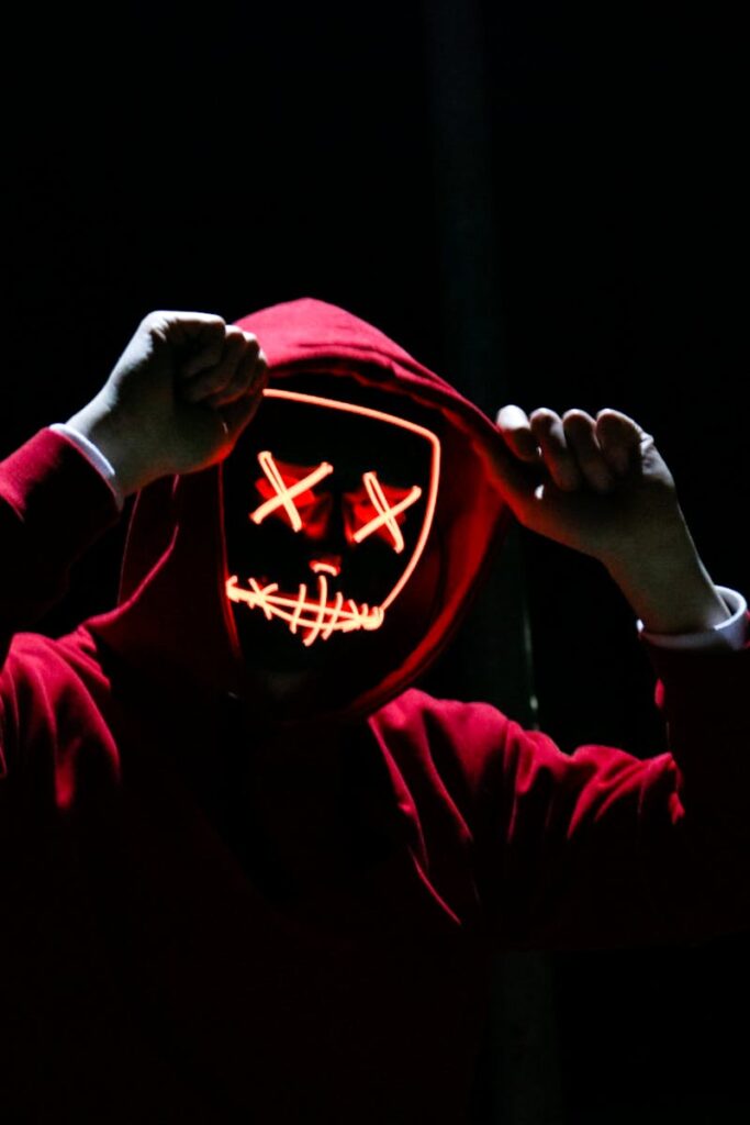 A spooky illuminated mask figure with a red hoodie in a dark setting, perfect for Halloween themes.