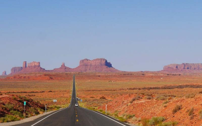 Long straight road through Monument Valley with red rock formations under a clear blue sky.