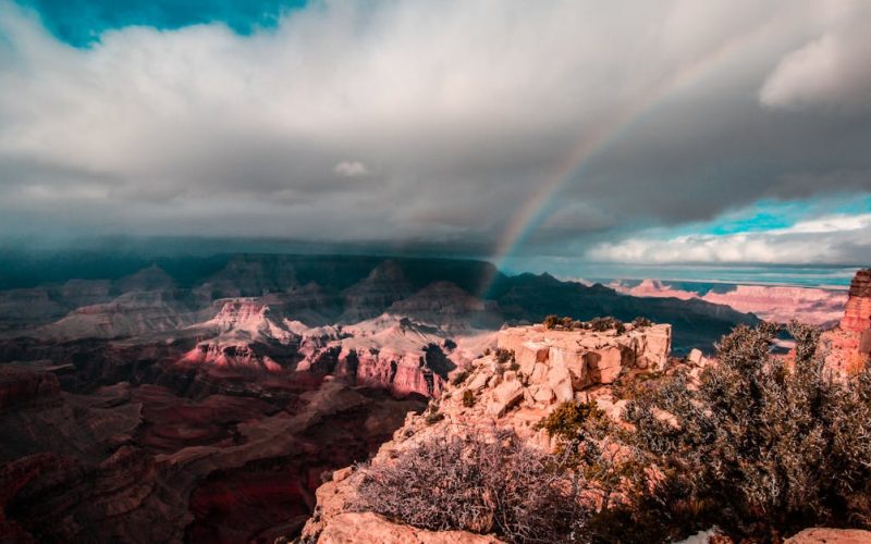 Stunning view of a rainbow arching over the Grand Canyon, capturing the majestic red rock formations under a dramatic sky.